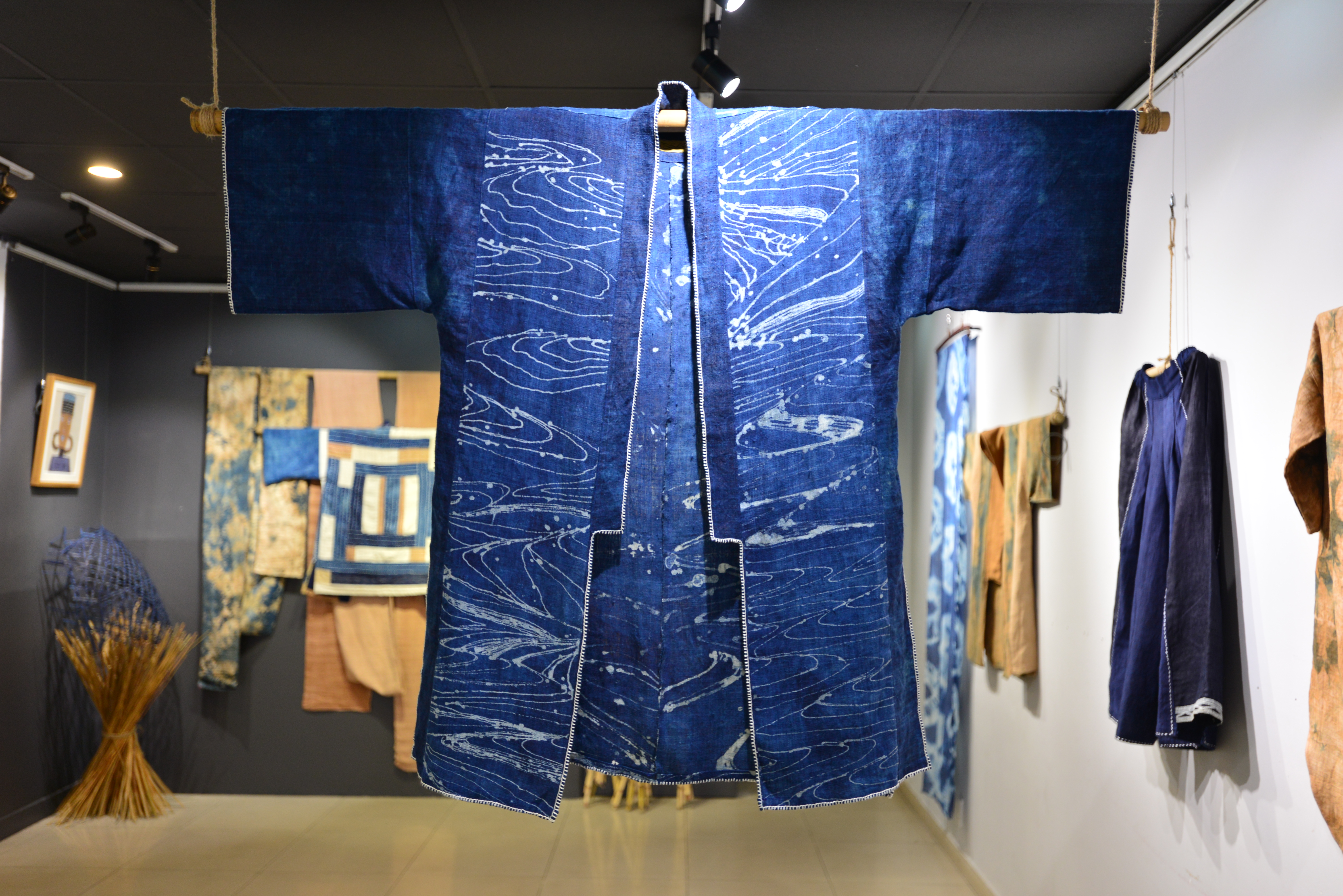 An indigo-coloured coat that is hanging from the ceiling with arms outspread. The fabric itself has a white pattern on it that looks a little like waves or a topographical map.